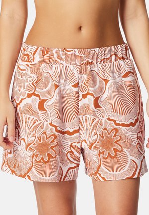 Vrouw draagt witte shorts met een oranje schelpenpatroon, voorzien van een elastische tailleband en zijzakken.