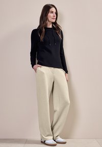 Svart hooded sweatshirt med dragsko, parat med ljusbeige vida byxor. Vita sneakers med bruna sulor och svarta detaljer.