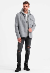 Veste en mélange de laine grise avec un devant à boutons, assortie à un sweat à capuche gris, un jean noir déchiré et des bottes noires à lacets.