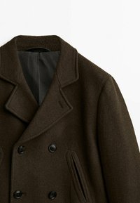 Cappotto in lana marrone con un classico design doppiopetto, grandi bottoni neri e tasche laterali con una fodera testurizzata.