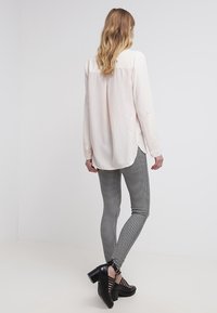 Camicia lunga rosa chiaro con orlo curvo, abbinata a leggings a scacchi bianco e nero e scarpe con tacco chunky nere.