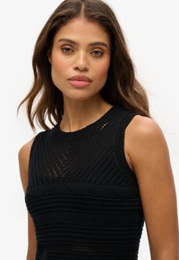 Haut sans manches en tricot noir avec des motifs texturés, des bords côtelés et un design en trame ouverte subtil pour la respirabilité et le style.