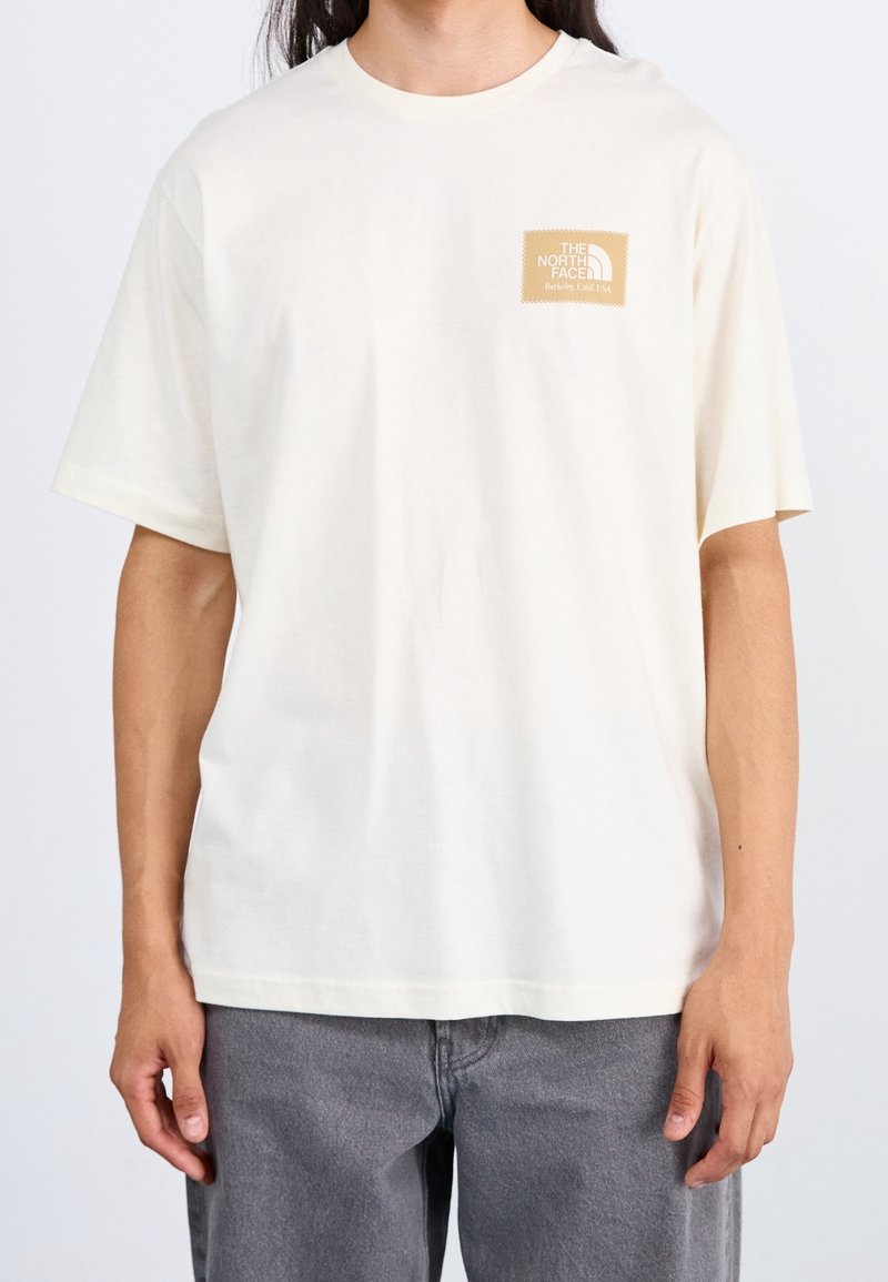 Kortärmad, krämfärgad bomull t-shirt med en rektangulär, beige logopatch med texten "The North Face" på vänster bröst.