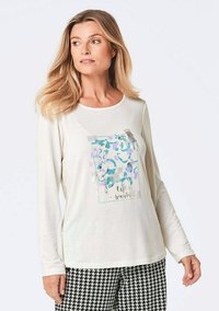 Langärmliges, crèmefarbenes T-Shirt mit mehrfarbigem Grafikdruck voller Tiermuster und silbernen Akzenten, kombiniert mit Hahnentrittmuster-Hosen.