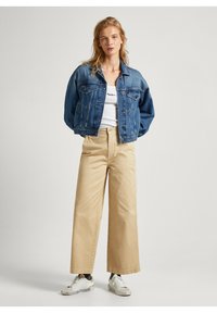 Jeans jakna s opuštenim krojem, svijetloplava boja, dva džepa na prsima, uparen s bež hlačama širokih nogavica visokog struka i bijelim tenisicama.