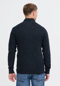 Dunkelgrauer, gestrickter Pullover mit hohem Kragen, gerippten Bündchen und Saum. Hat einen lässigen Schnitt und ist von hinten vor einem schlichten Hintergrund zu sehen.
