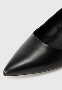 Svart högklackad sko med spetsig tå, slätt syntetiskt material och en lågt skuren design för en elegant silhuett.