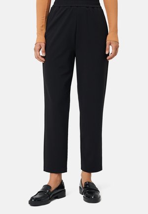 Pantaloni neri con vita elastica e vestibilità dritta, caratterizzati da una consistenza liscia. Abbinati a mocassini neri lucidi per un contrasto.