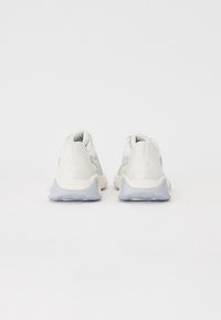 Pár bílých sportovních bot se šedými podrážkami pohledem zezadu na čistém bílém pozadí.