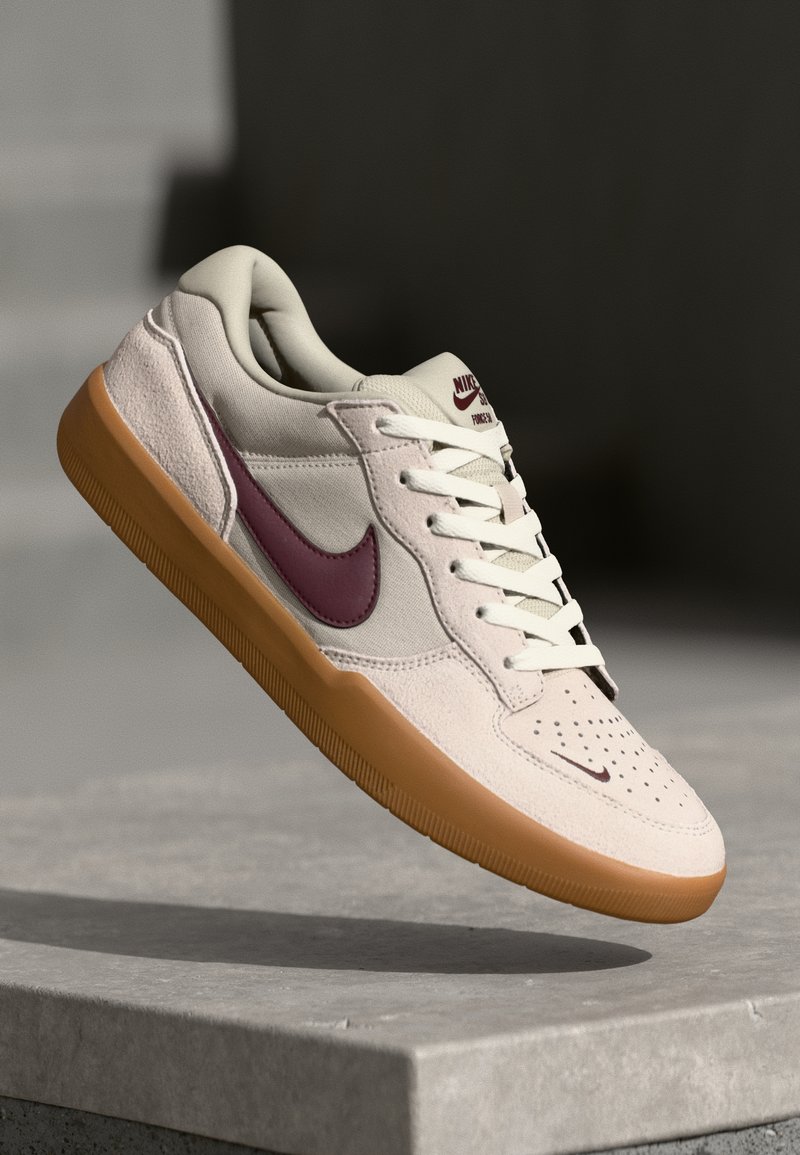 Tenisky Nike s krémovým zamakom, bordo swooshom, perforovanou špičkou a gumovou podrážkou. Šnurovací dizajn s polstrovaným golierom.