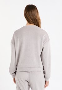 Felpa grigia a coste con scollo rotondo, spalle cadenti e maniche lunghe. Il tessuto ha un aspetto morbido e strutturato.