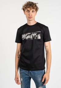 Camiseta de manga corta negra hecha de algodón, con un diseño gráfico de texto plateado en el pecho. Textura suave, cuello redondo clásico.