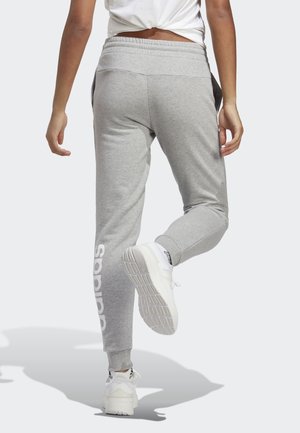 Grijze joggingbroek met een smal lopende pijp, elastische tailleband en wit "adidas" logo aan de rechterkant. Gecombineerd met witte sportschoenen.