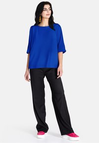 Blusa oversize blu con maniche corte abbinata a pantaloni neri a gamba larga e sneakers rosa. Tessuto morbido con un design a tinta unita.