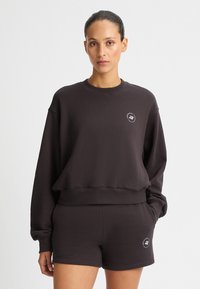 Completo con felpa nera e pantaloni corti, realizzato in tessuto morbido. La felpa ha un colletto tondo e un dettaglio del logo sul petto. Vestibilità casual e rilassata.