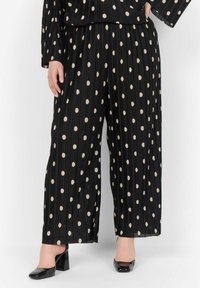 Schwarze, plissierte, weit geschnittene Hosen mit großen beigen Polka-Dots. Zu den Details gehören ein bequemer Bund, kombiniert mit schwarzen High Heels.