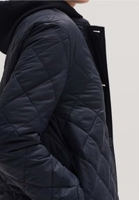 Laivastonsininen pehmustettu takki, jossa on tekstuuripinta, musta huppu, nappikiinnitys ja vinoraitamusteri.