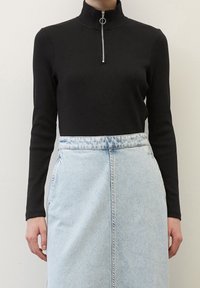 Maglietta a maniche lunghe nera a costine con colletto alto e zip argentata. Abbinata a una gonna di jeans azzurri chiari con cucitura frontale.