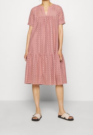 Lyserød kjole med korte ærmer, V-hals, hulmønster og lagdelt design, kombineret med lyse sandaler med spænde detaljer.