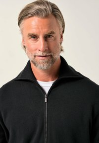 Černý svetr na zip s vysokým límcem, s hladkou strukturou a minimálním zdobením. Nosený přes bílou košili.