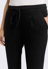 Zwarte gewatteerde joggingbroeken met een elastische tailleband, voorzien van zijkleppen en subtiele plooien voor extra detail.