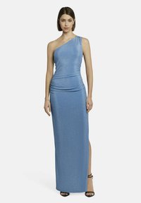 Ein einseitig geschnittenes blaues Kleid aus glänzendem Stoff, das über Raffung an der Taille, einen seitlichen Schlitz verfügt und mit schwarzen Riemchenhighheels getragen wird.