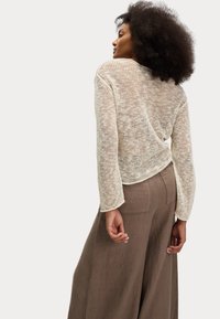Pull en maille ivoire avec des manches longues, design en tissage ouvert et ourlet arrondi, associé à un pantalon en lin marron ample.