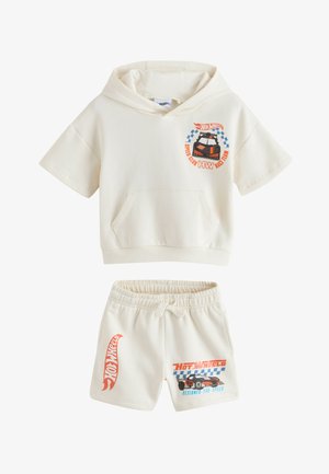 Conjunto de sudadera con capucha de manga corta y pantalones cortos en color crema con logotipos de Hot Wheels, gráfico de coche de carreras y diseños de bandera a cuadros en pecho y pierna.