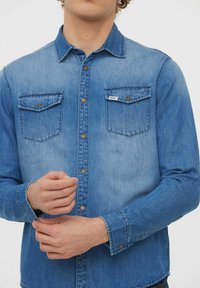 Chemise en denim à manches longues, dégradé de bleu clair à bleu foncé, avec un devant boutonné, deux poches poitrine et des boutons en métal, offrant une coupe décontractée.