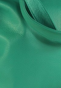 Groene leren draagtas met een gestructureerd oppervlak en een glad handvat. Het ontwerp heeft afgeronde randen en een ruim interieur.