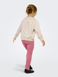 Lichtbeige sweatshirt met kleurrijke bloemenborduursels, gecombineerd met aansluitende roze ribgebreide leggings en zwarte ballerina's.