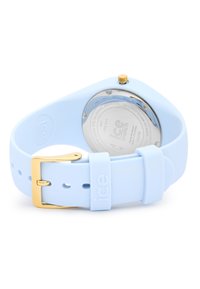 Montre en silicone bleu clair avec une boucle dorée, un cadran rond et un dos en argent. Le design présente une texture lisse et des accents minimaux.