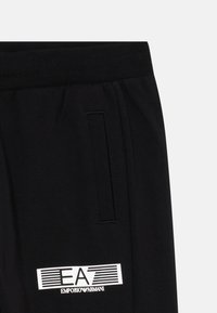 Schwarze Emporio Armani Sweatpants mit elastischem Bund, seitlichem Taschen und weißem EA-Logo nah dem Saum.