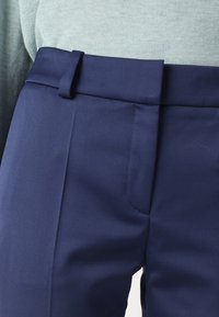 Námořnické modré kalhoty na míru s hladkým, texturovaným materiálem, vybavené poutkem na opasek, švem kapsy a rovně střiženým designem.