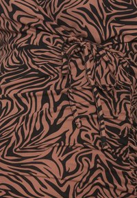Gros plan sur un tissu marron avec des rayures zébrées noires et un détail de ficelle nouée au centre.
