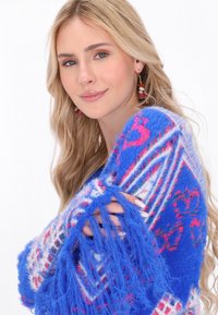 Pulover albastru pufoasă cu modele vibrante roz și alb, margine ciufulită și o textură moale. Remarcabil pentru culoarea și designul său îndrăzneț.