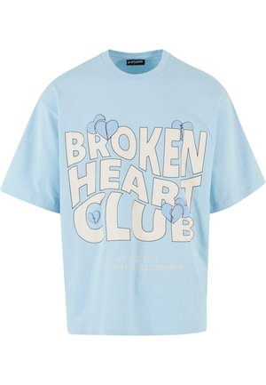 Camiseta de algodón de color azul claro con mangas cortas, que presenta una gran impresión de "BROKEN HEART CLUB" en letras blancas en negrita y corazones azules.