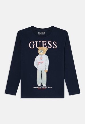 Granatowa koszula z długim rękawem z logo GUESS, z nadrukiem misia w bluzie z kapturem i spodniach oraz tekstem "Original Authentic Brand Est. 1981."