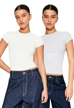 Due t-shirt aderenti, una bianca e una grigio chiaro, realizzate in un tessuto liscio con maniche corte, abbinate a jeans di denim scuro a vita alta.