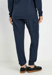 Granatowe, prążkowane spodnie dresowe z elastycznymi mankietami i bocznymi kieszeniami cargo, w zestawie z czarnymi trampkami z brązową podeszwą i białymi sznurowadłami.