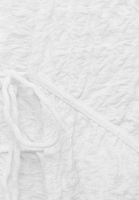 Gros plan sur un tissu blanc texturé avec des coutures côtelées et un détail de cordon noué sur un matériau doux.