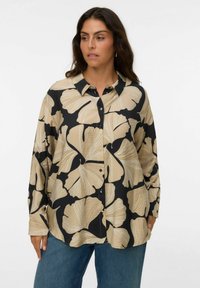 Chemise à boutons avec un fond noir ornée de grands motifs floraux beiges. Fabriquée en tissu léger, avec un col et des manches longues.