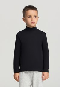 Czarny golf z długim rękawem wykonany z gładkiego materiału, z dopasowanymi rękawami i prostym dołem, noszony z jasnoszarymi spodniami dresowymi.