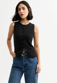 Zwarte geribbelde mouwloze top met een knoopsluiting aan de voorkant, ronde halslijn en zijsplitten; gecombineerd met hoge blauwe denim jeans.