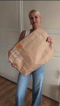 Donna in top bianco e jeans blu che tiene una grande busta di carta marrone con la scritta "Amami. Indossami." e il logo Zalando.