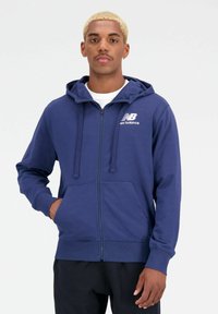 Marine blauwe hoodie met rits, met aantrekkoord, voorzakken, geribbelde manchetten en het witte New Balance-logo op de linkerborst. Gemaakt van zachte katoenmix.