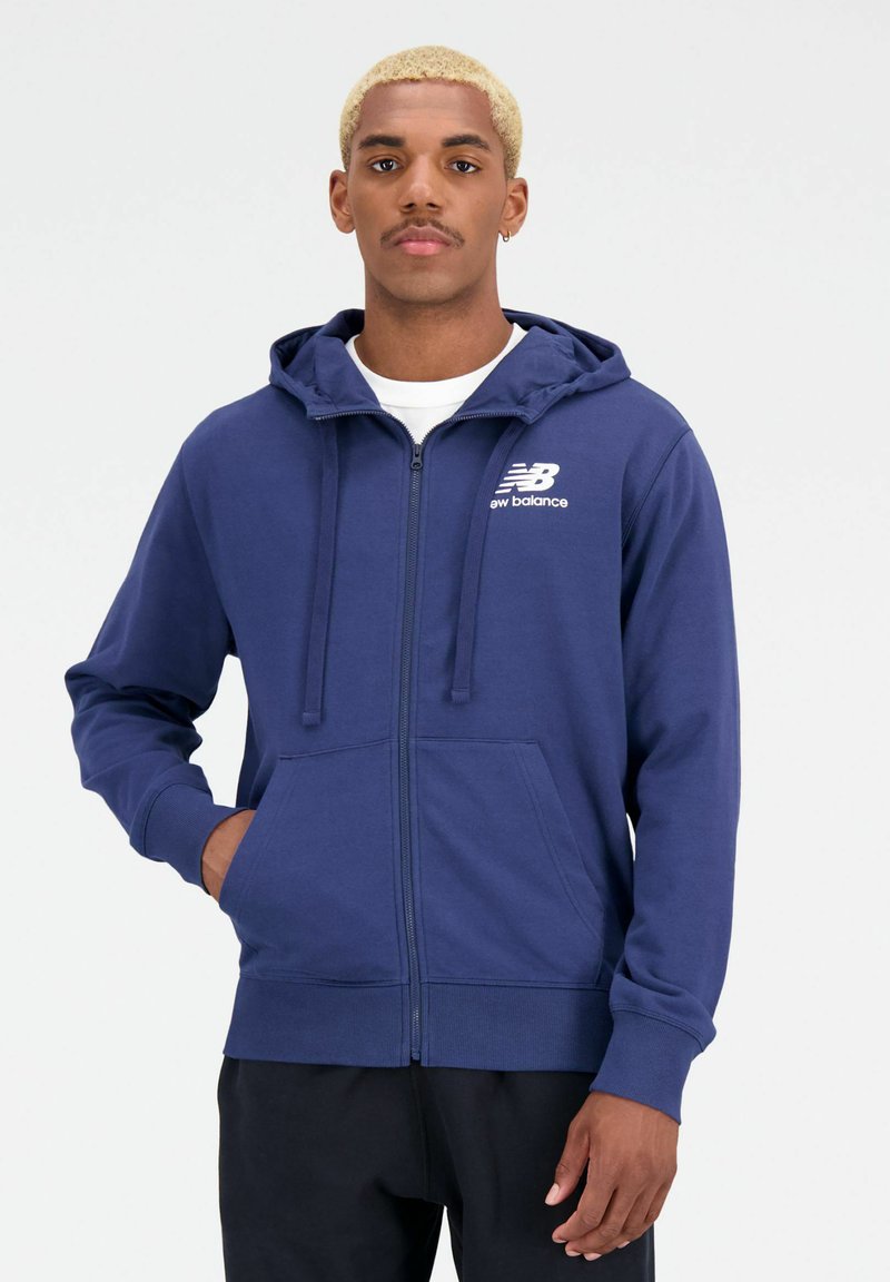 Marine blauwe hoodie met rits, met aantrekkoord, voorzakken, geribbelde manchetten en het witte New Balance-logo op de linkerborst. Gemaakt van zachte katoenmix.