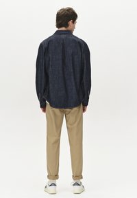 Dunkelblaus Denim-Hemd mit langen Ärmeln, Kragen und Knopfmanschetten, kombiniert mit khakifarbenen Hosen und weißen Turnschuhen mit blauen Akzenten.