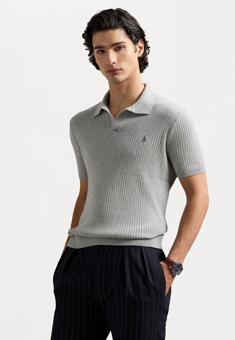 Grijze polo met korte mouwen en ribbeltextuur, voorzien van een kraag en geborduurd logo. Gecombineerd met donkere broek met pinstripe.