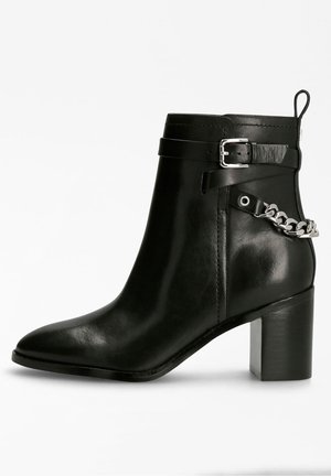 Bottine en cuir noir à bout rond, avec un talon bloc proéminent, une sangle à boucle sur le côté et un accent en chaîne argentée à la cheville.